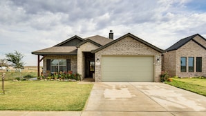 A two-story house with a garage, brick exterior, and a well-maintained lawn. - 11 Mi to Texas Tech University: Cozy Family Home! (Wolfforth)