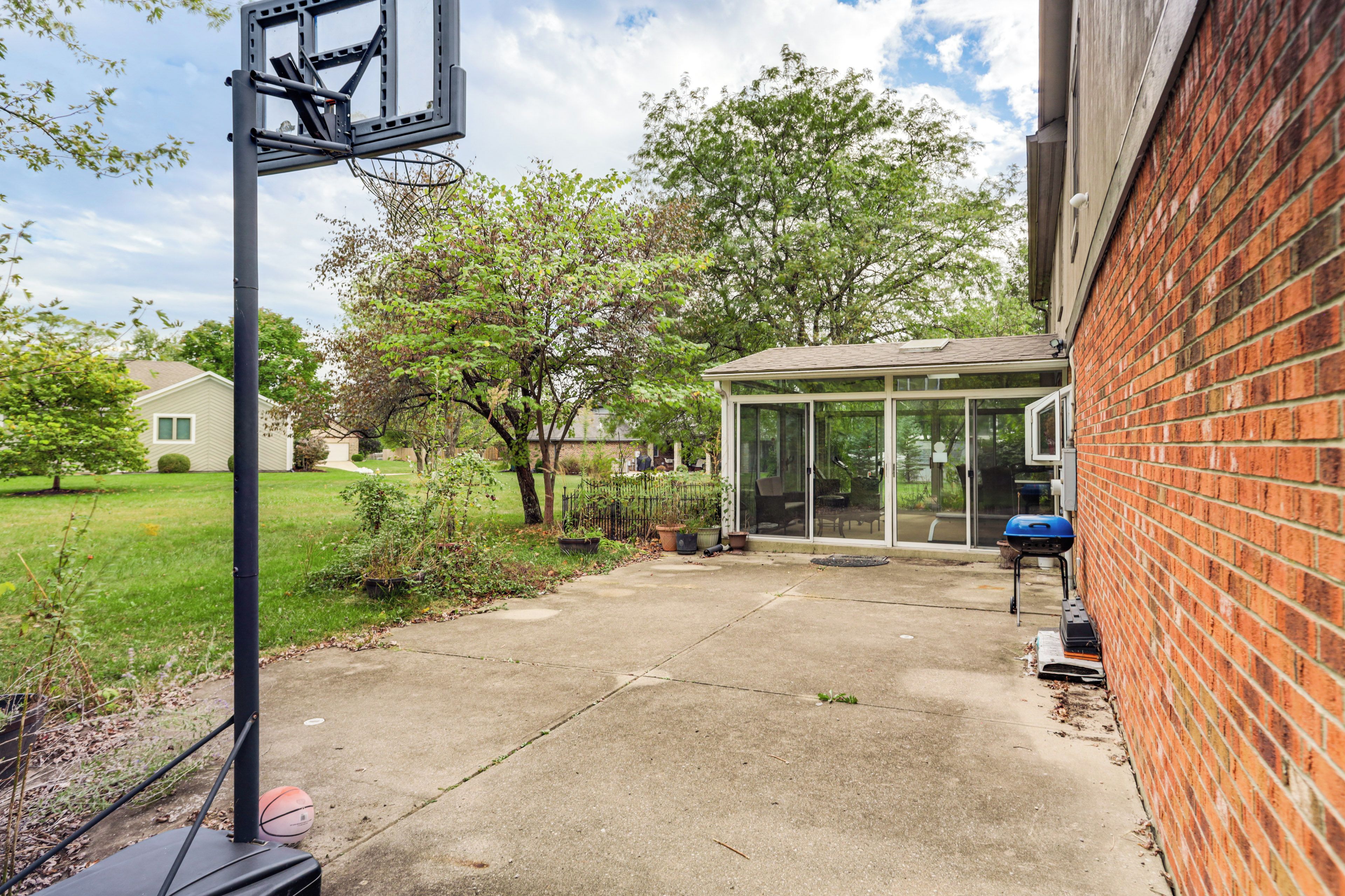A backyard with a basketball hoop, a glass enclosure, and a brick wall.