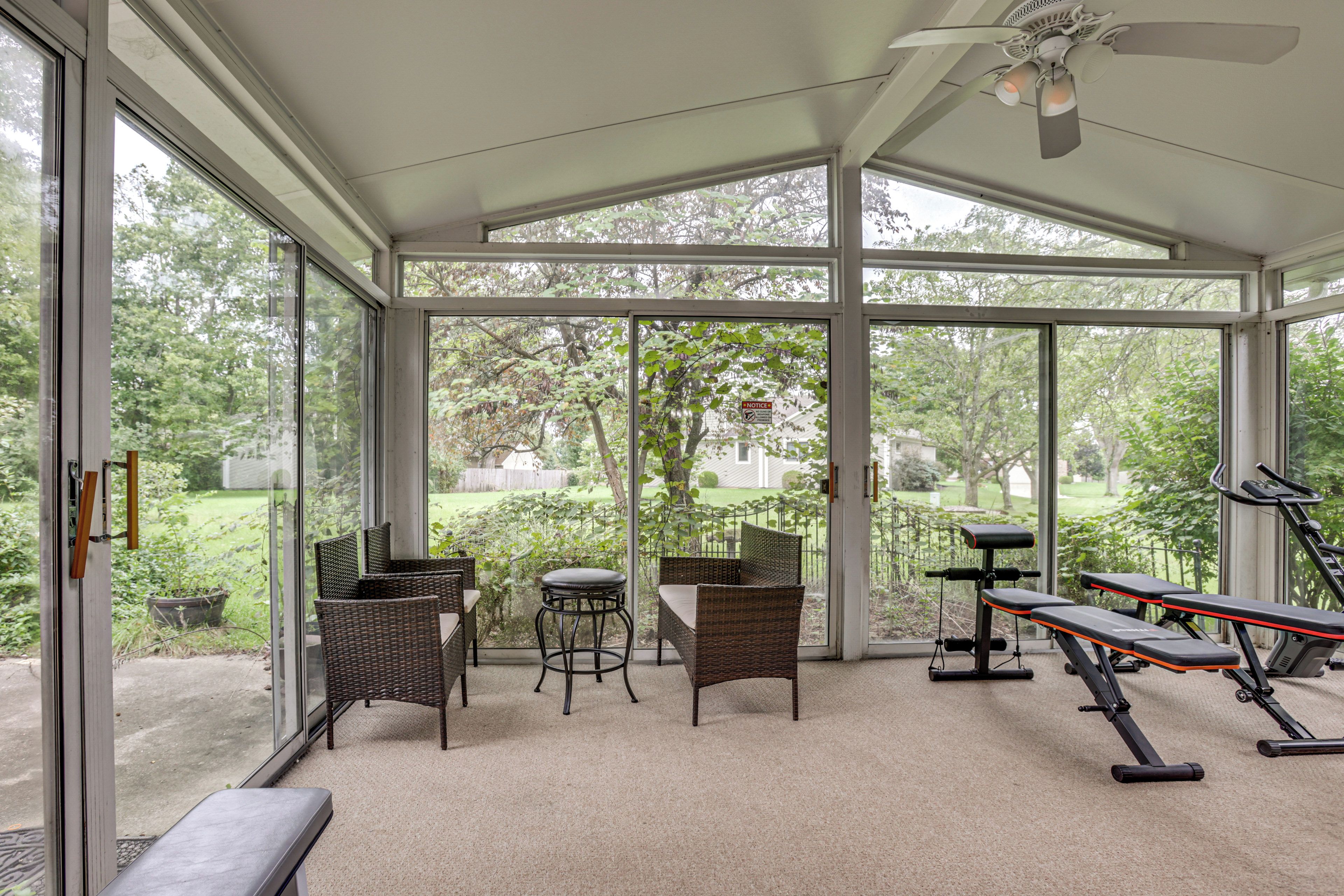 A sunroom with large windows, wicker furniture, and exercise equipment.