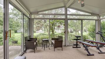 A sunroom with large windows, wicker furniture, and exercise equipment.