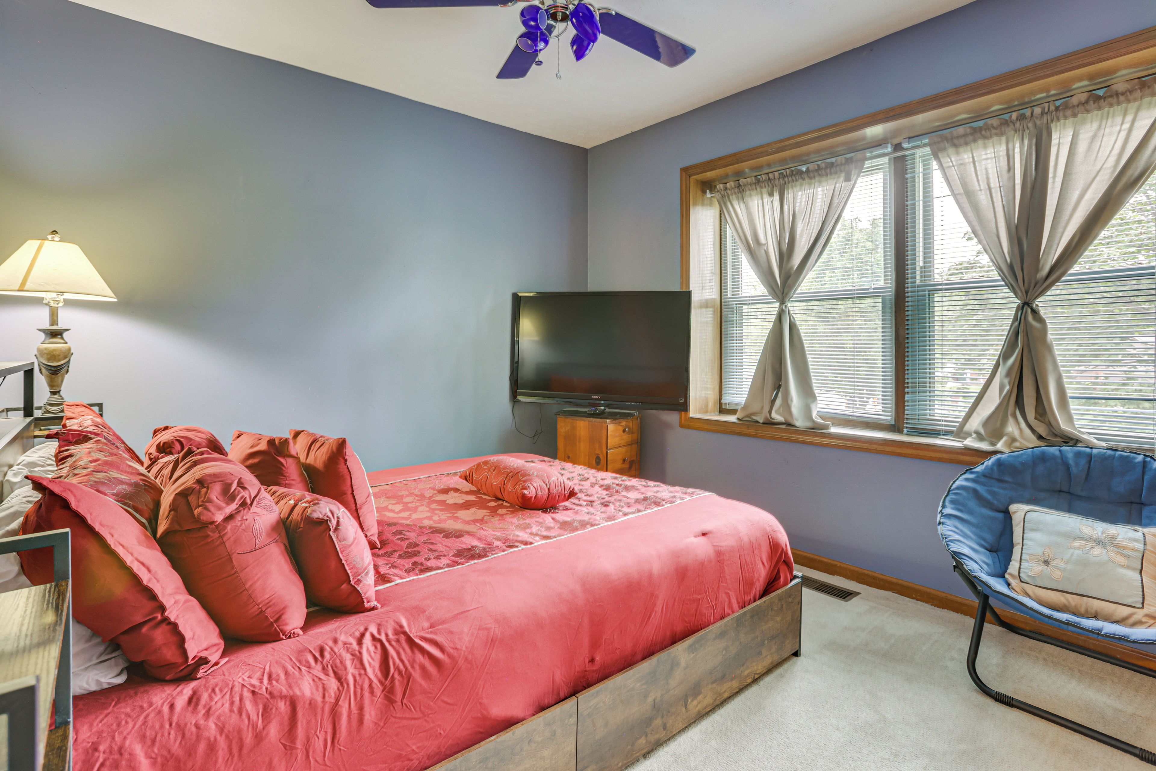 A bedroom with a bed, a television, a lamp, a chair, and a window with curtains.