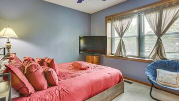 A bedroom with a bed, a television, a lamp, a chair, and a window with curtains.