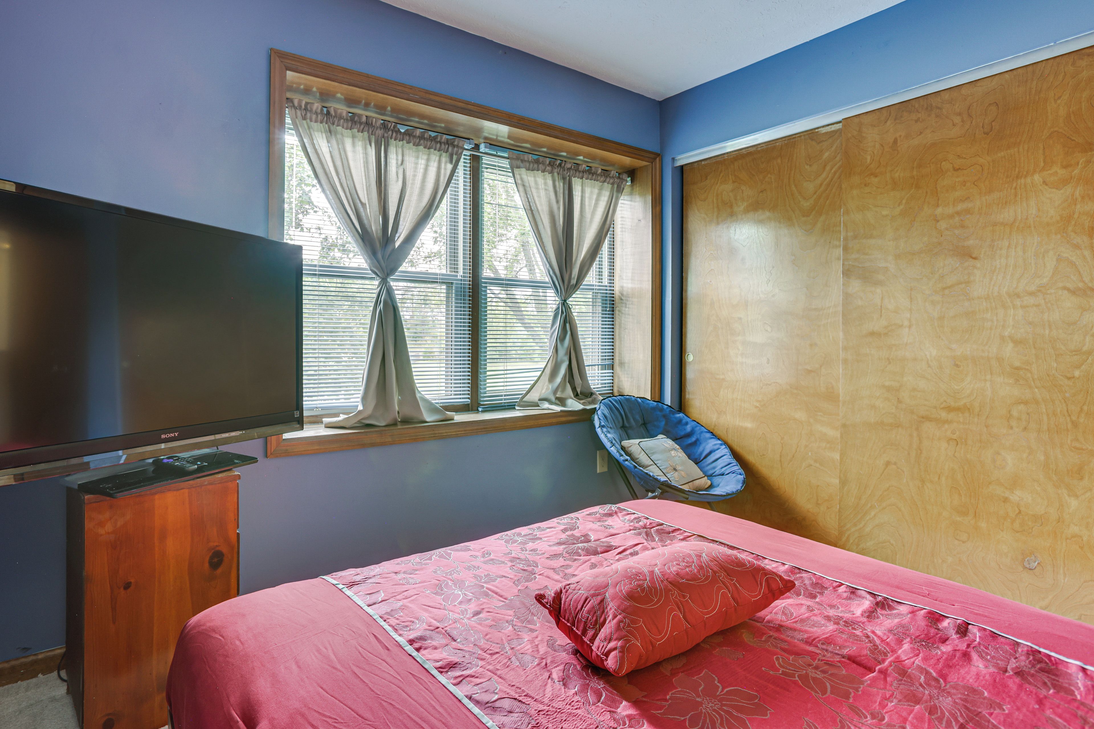 Une chambre à coucher avec un lit, une télévision, une fenêtre avec des rideaux et une armoire en bois.