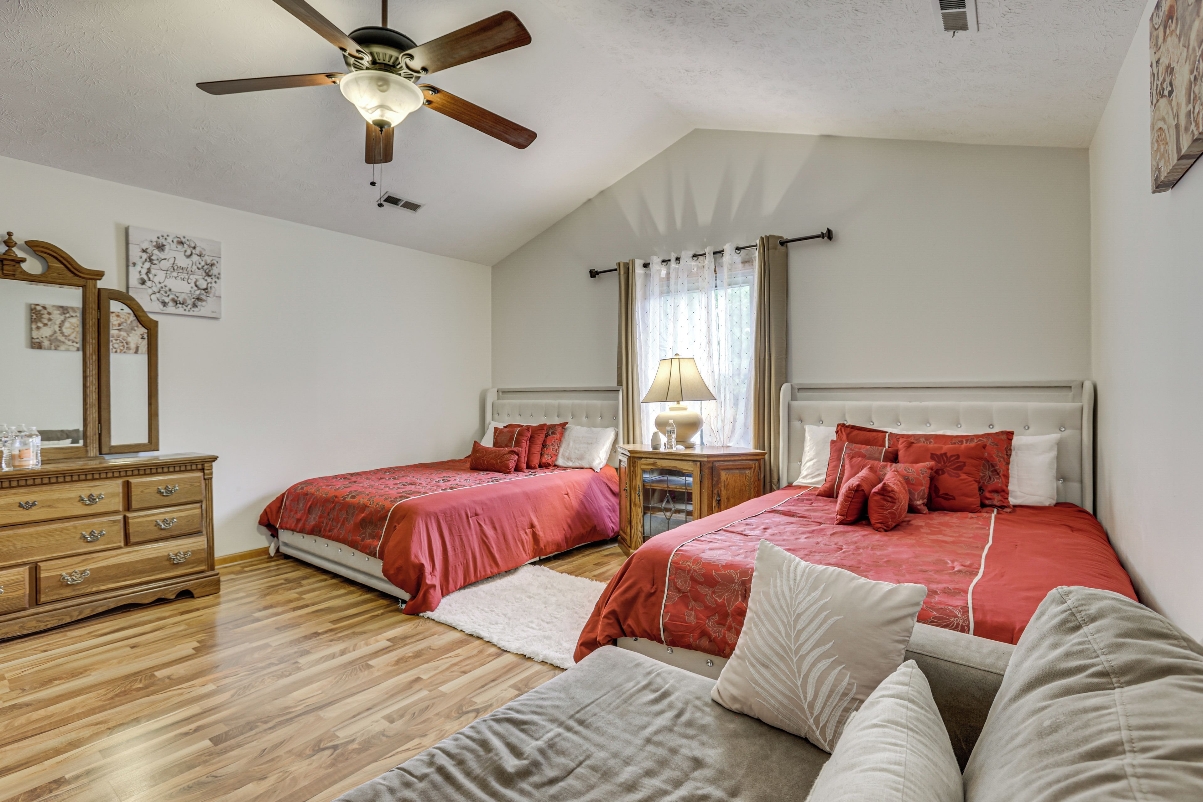 A bedroom with two beds, wooden furniture, a ceiling fan, and a window with curtains.