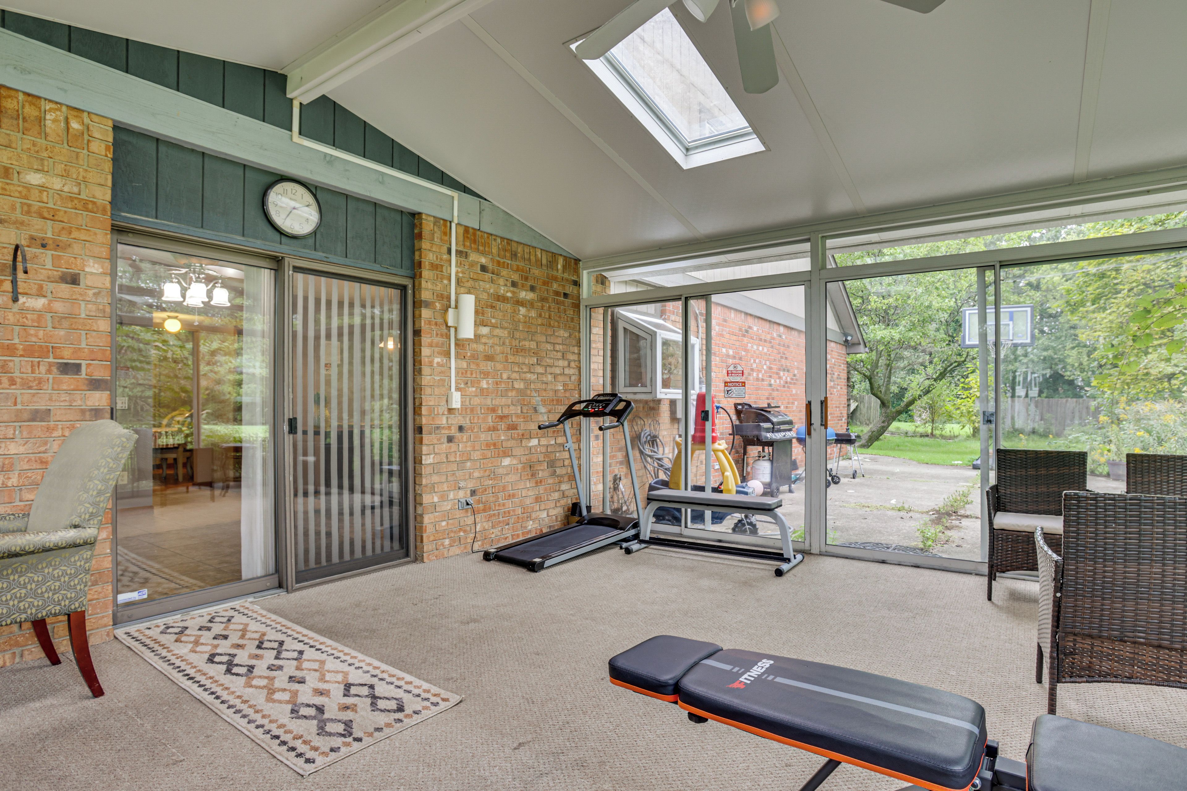 A home gym with exercise equipment, a clock, and a view of the outdoors.