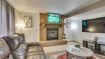 A living room with a leather sofa, a fireplace, a television, and a flat-screen TV mounted on the wall.