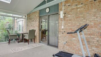 A room with a brick wall, a sliding glass door, a treadmill, and a dining area with chairs and a table.