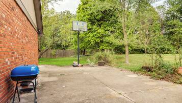 A backyard with a basketball hoop, a barbecue grill, and a brick wall.