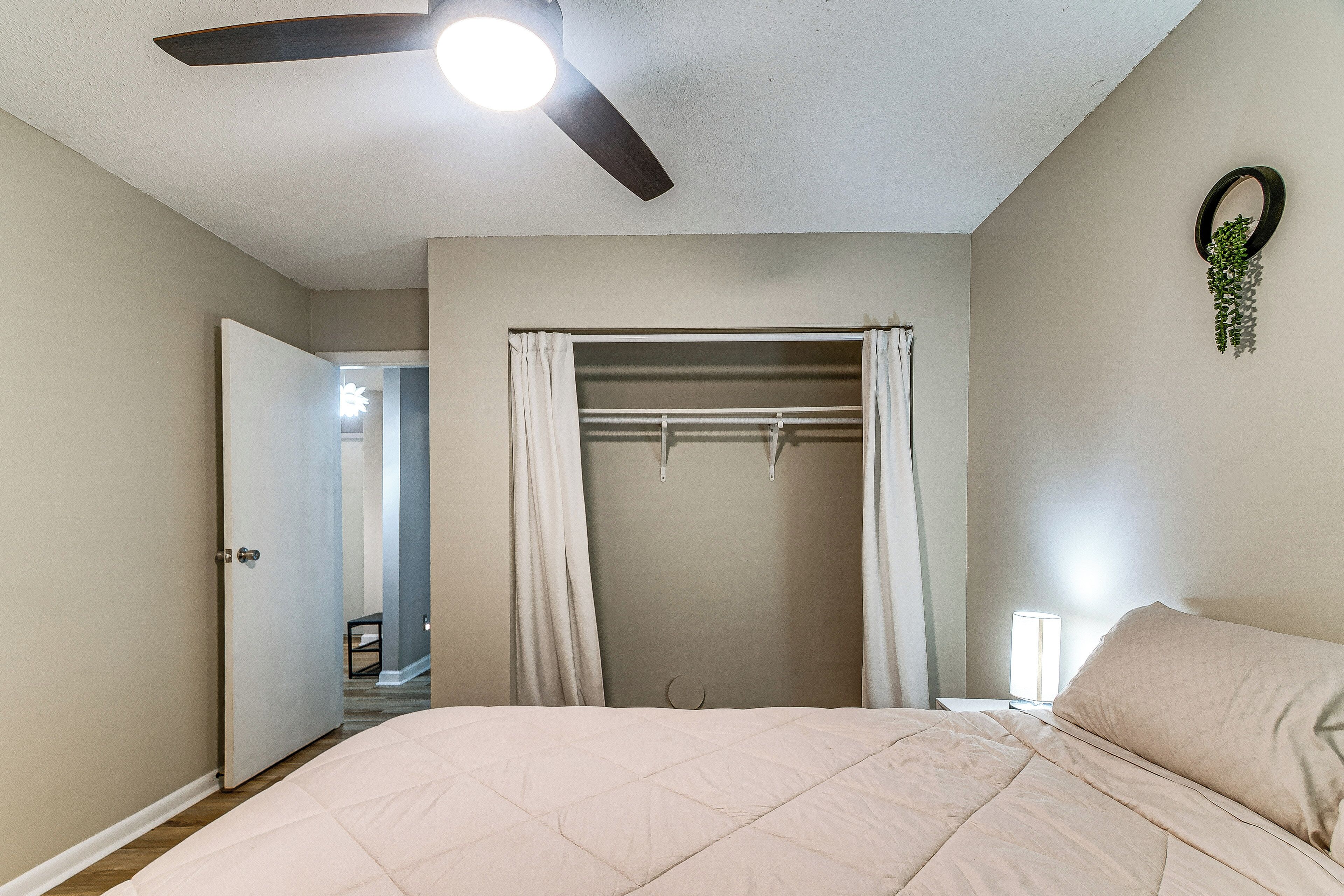 A bedroom with a bed, a ceiling fan, a window with curtains, and a wall-mounted plant.