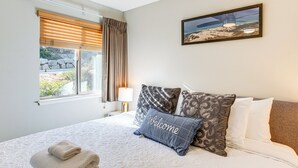 A neatly made bed with a 'Welcome' pillow, a window with blinds, and a framed picture on the wall. - 1 Mi to Stagecoach Chairlift: Stateline Condo (Stateline)