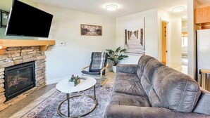A living room with a stone fireplace, a flat-screen TV, a gray sofa, a round coffee table, and a framed picture on the wall. - 1 Mi to Stagecoach Chairlift: Stateline Condo (Stateline)