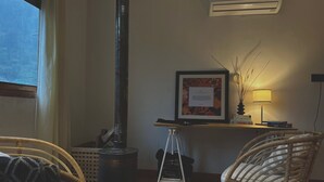 Una habitación acogedora con una estufa de leña, sillas de mimbre, un cuadro enmarcado y una lámpara sobre un escritorio.