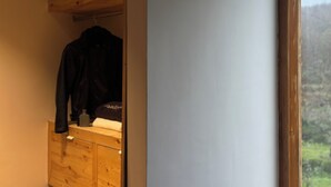 A wooden dresser with a hanging garment in a room with a view of a forested landscape through a window.