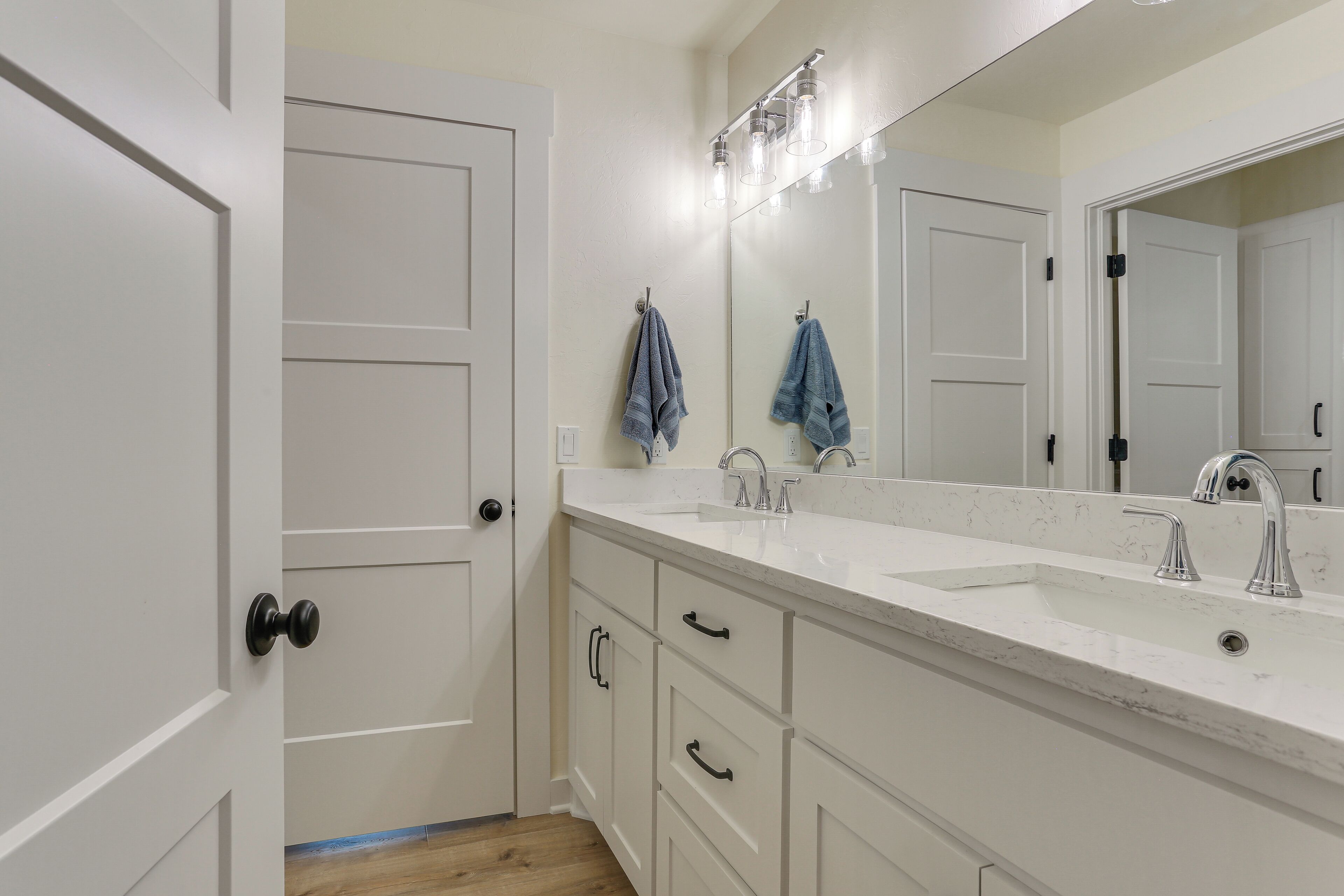 A bathroom with a white vanity, a double sink, and a large mirror with lights above.