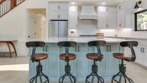 Eine moderne Küche mit weißen Schränken, einem Edelstahlkühlschrank und drei Barhocker mit Holzsitzen.