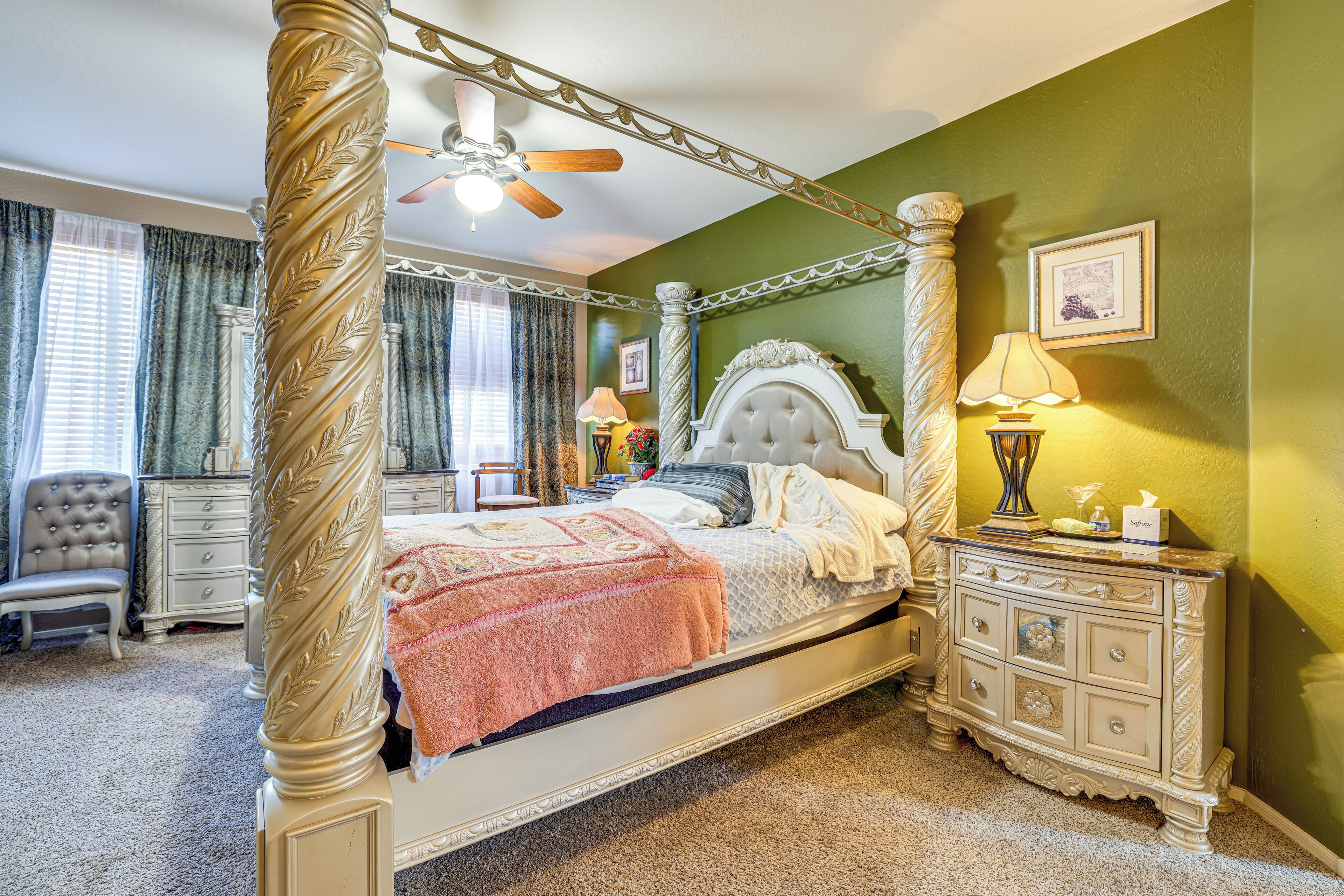A four-poster bed with a canopy, a nightstand with a lamp, and a chair in a room with green walls and a ceiling fan.