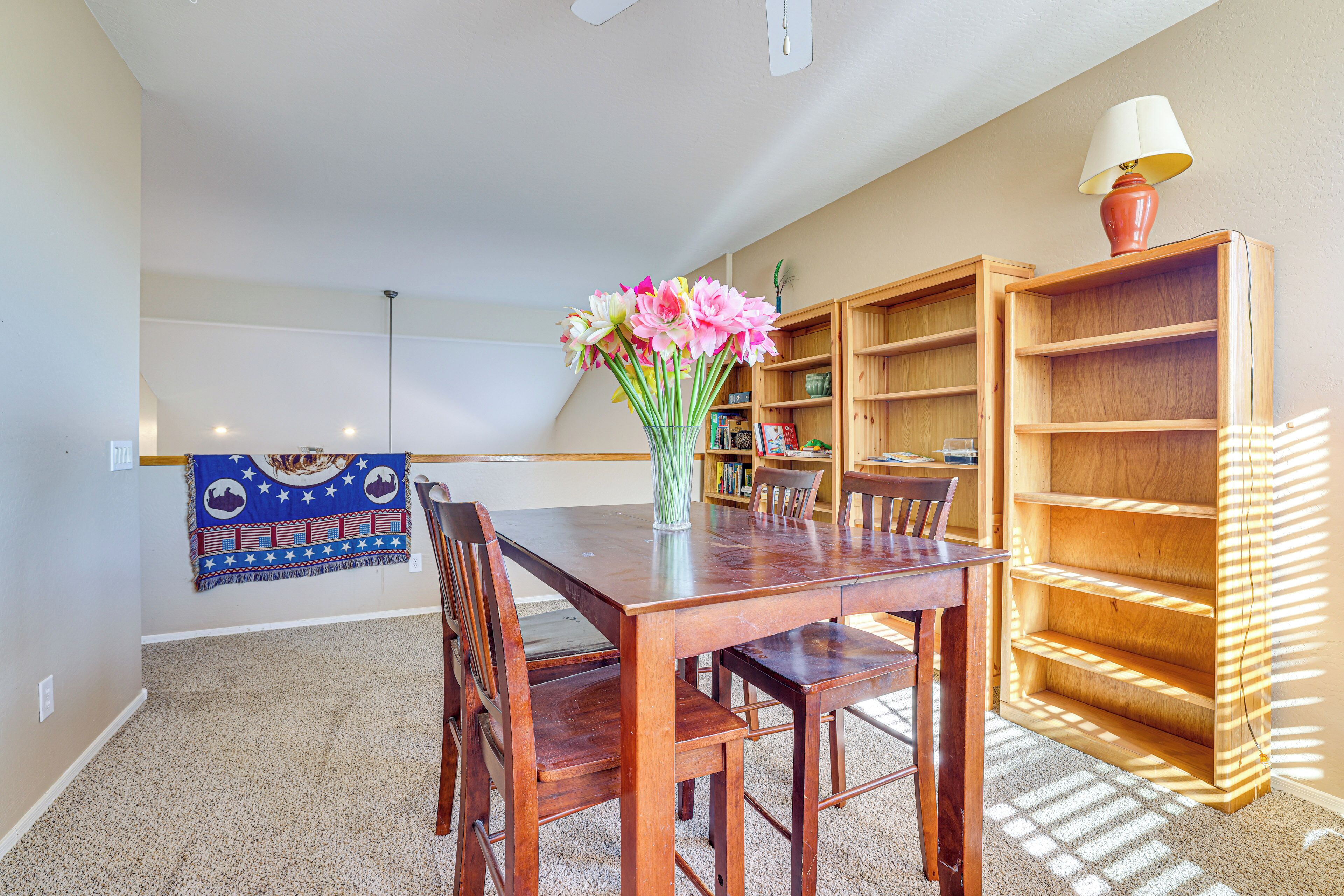 Un coin repas avec une table en bois, des chaises, un vase de fleurs et une bibliothèque.