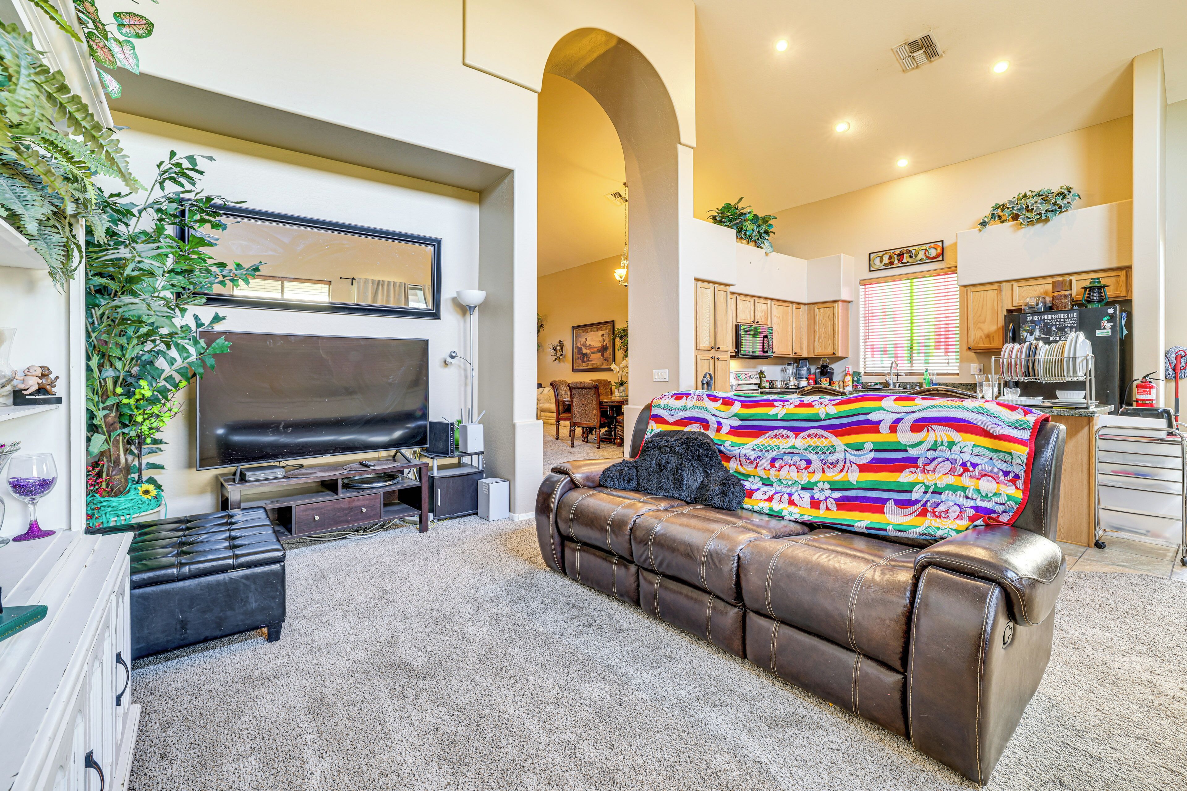 A living room with a brown leather sofa, a flat-screen TV, and a colorful blanket.