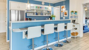 Una cocina con una decoración azul y blanca, electrodomésticos de acero inoxidable y taburetes de bar.