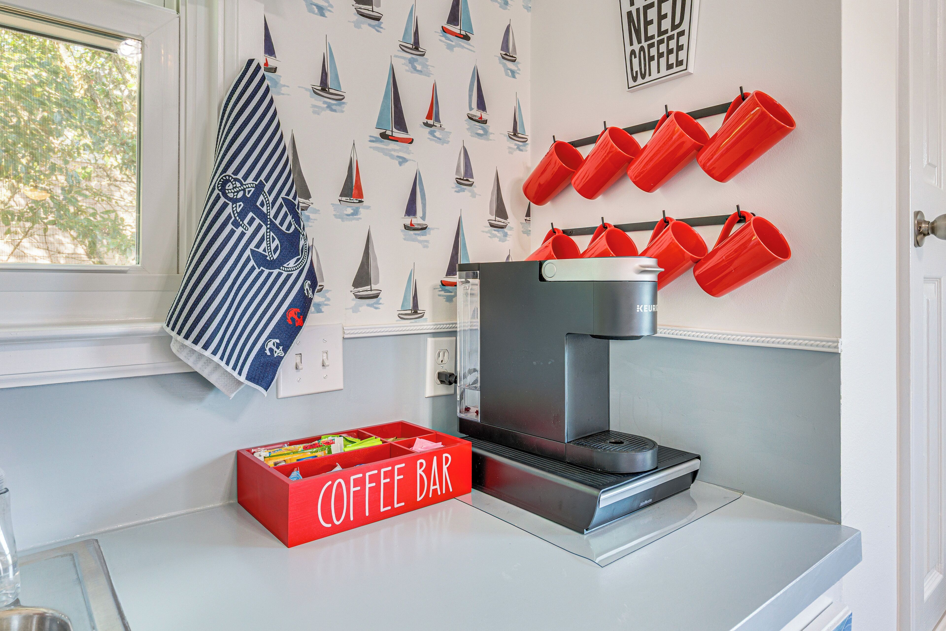 Una cocina con cafetera, tazas rojas y una barra para café.