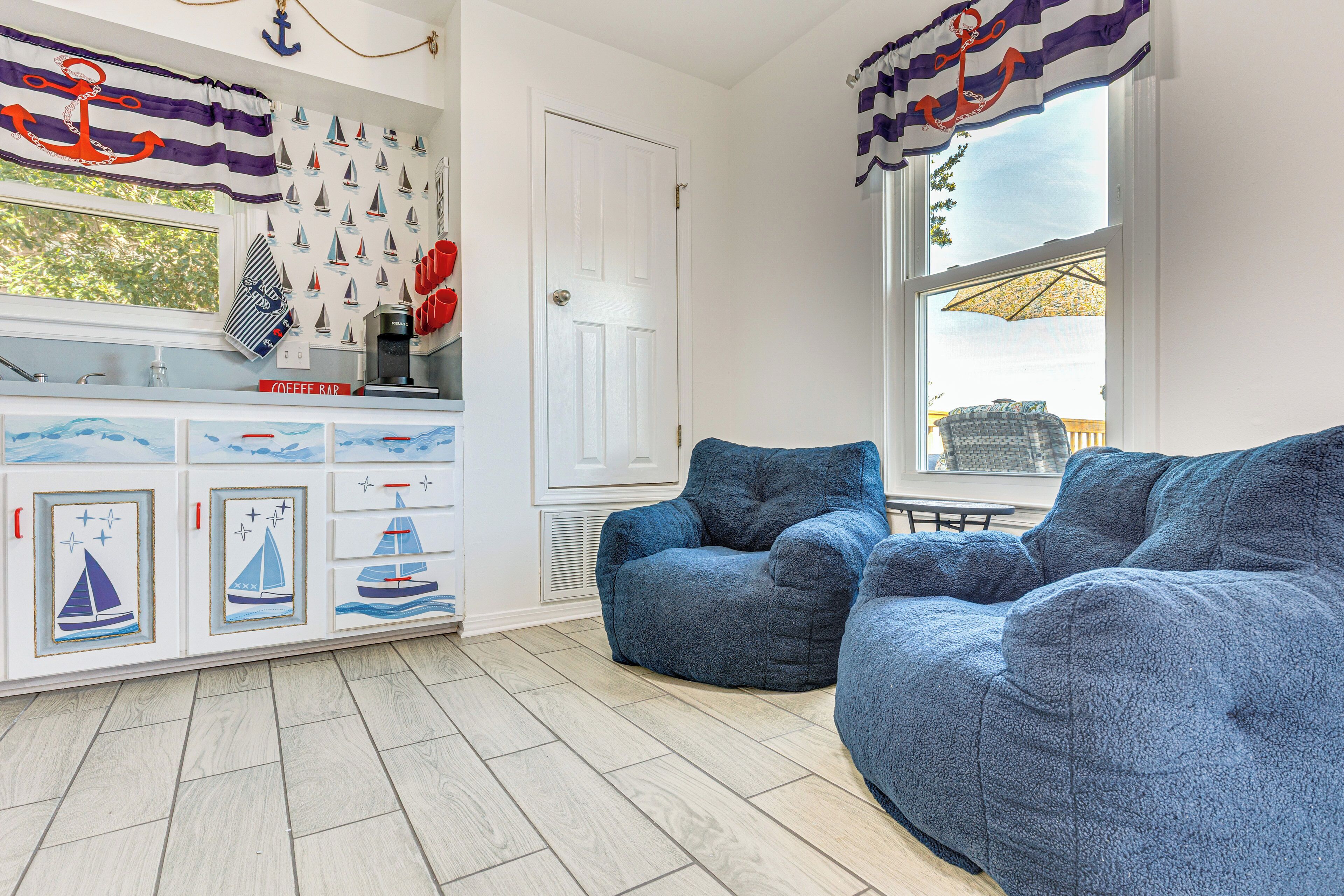 A cozy living room with a large blue sofa, a coffee bar with nautical-themed decor, and a window with a view of the outdoors.