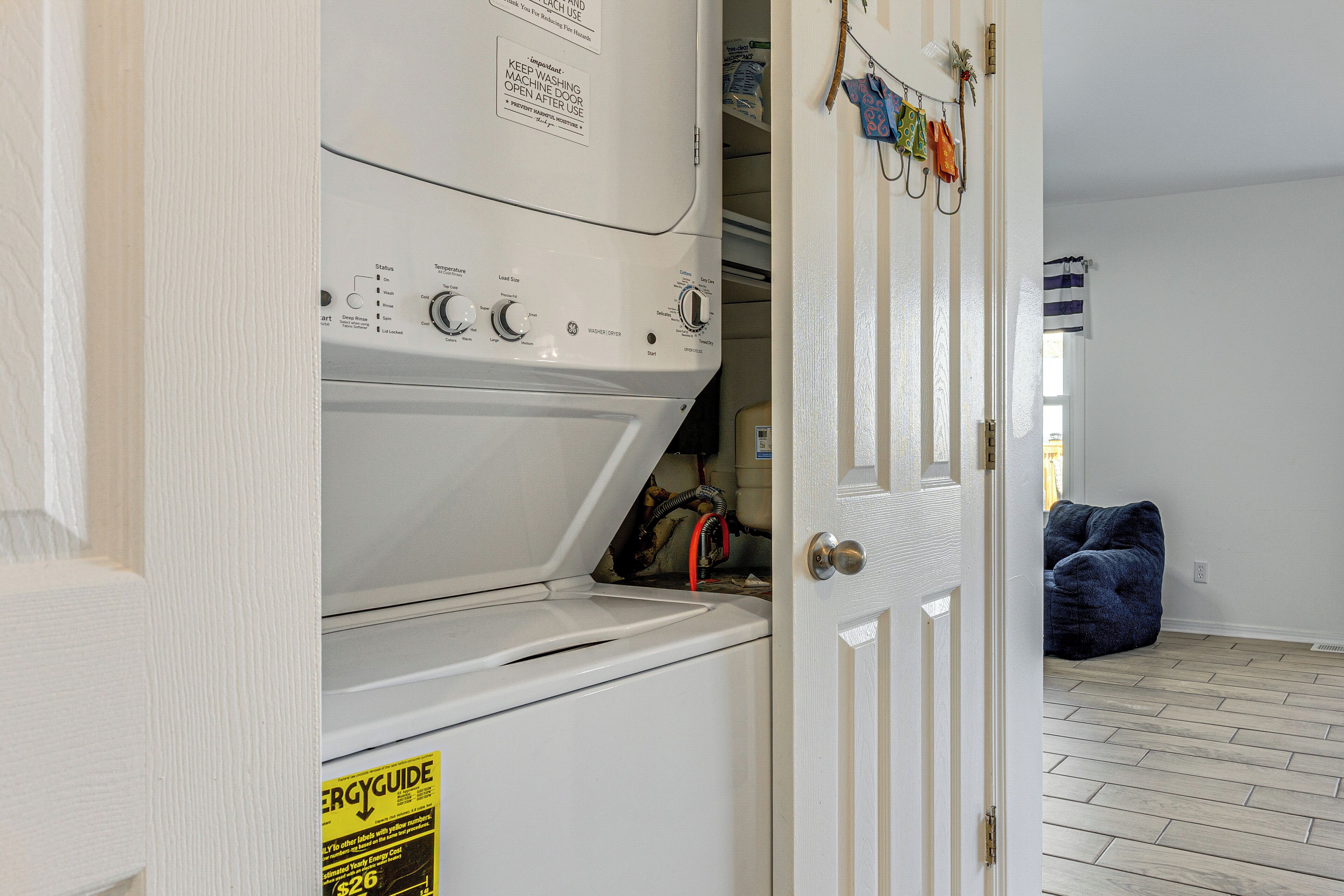 A laundry area with a front-loading washer and dryer, a door with a towel rack, and a blue chair in the adjacent room.