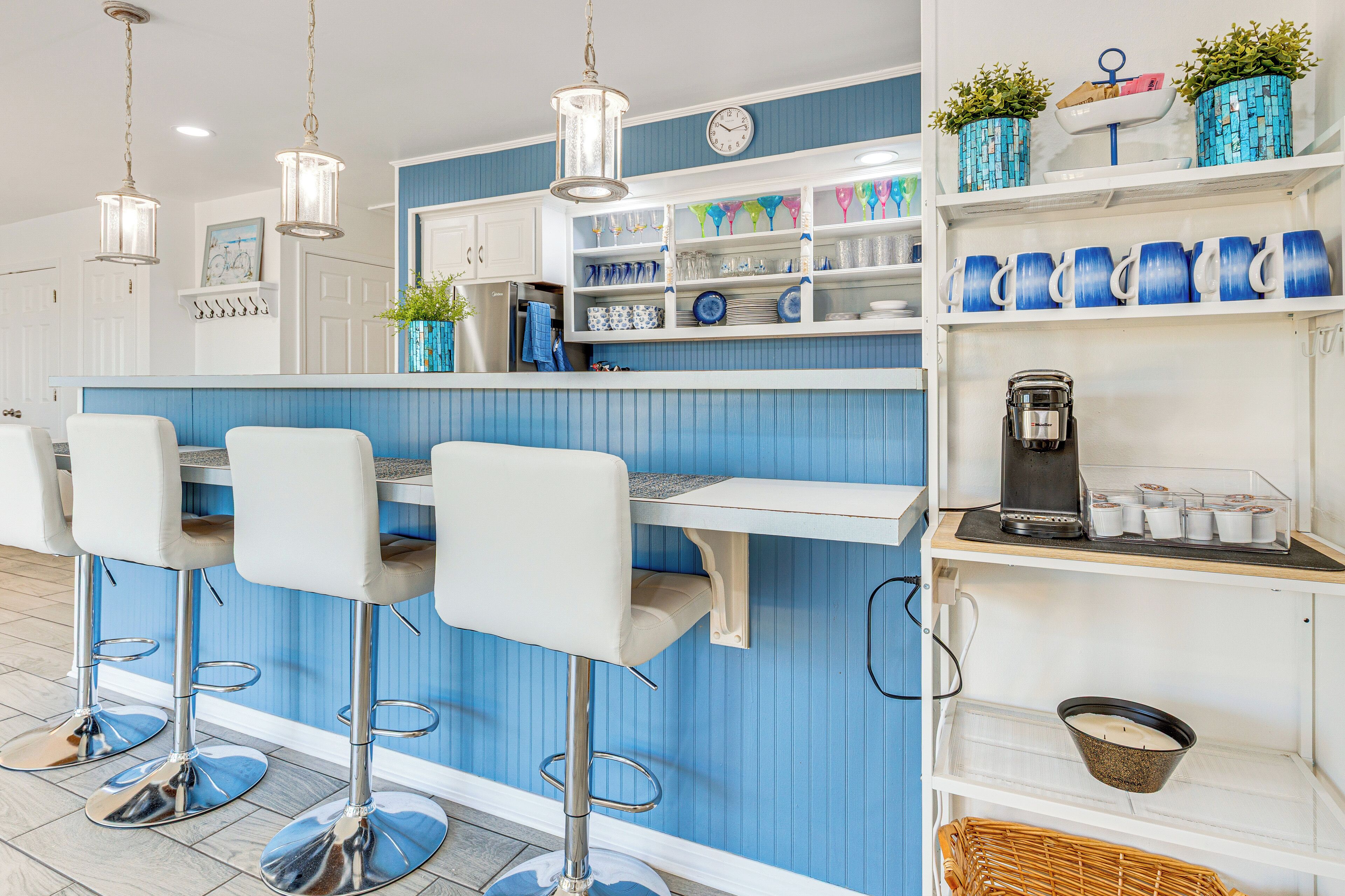 A bar area with white bar stools, a coffee machine, and shelves with blue mugs and plates.