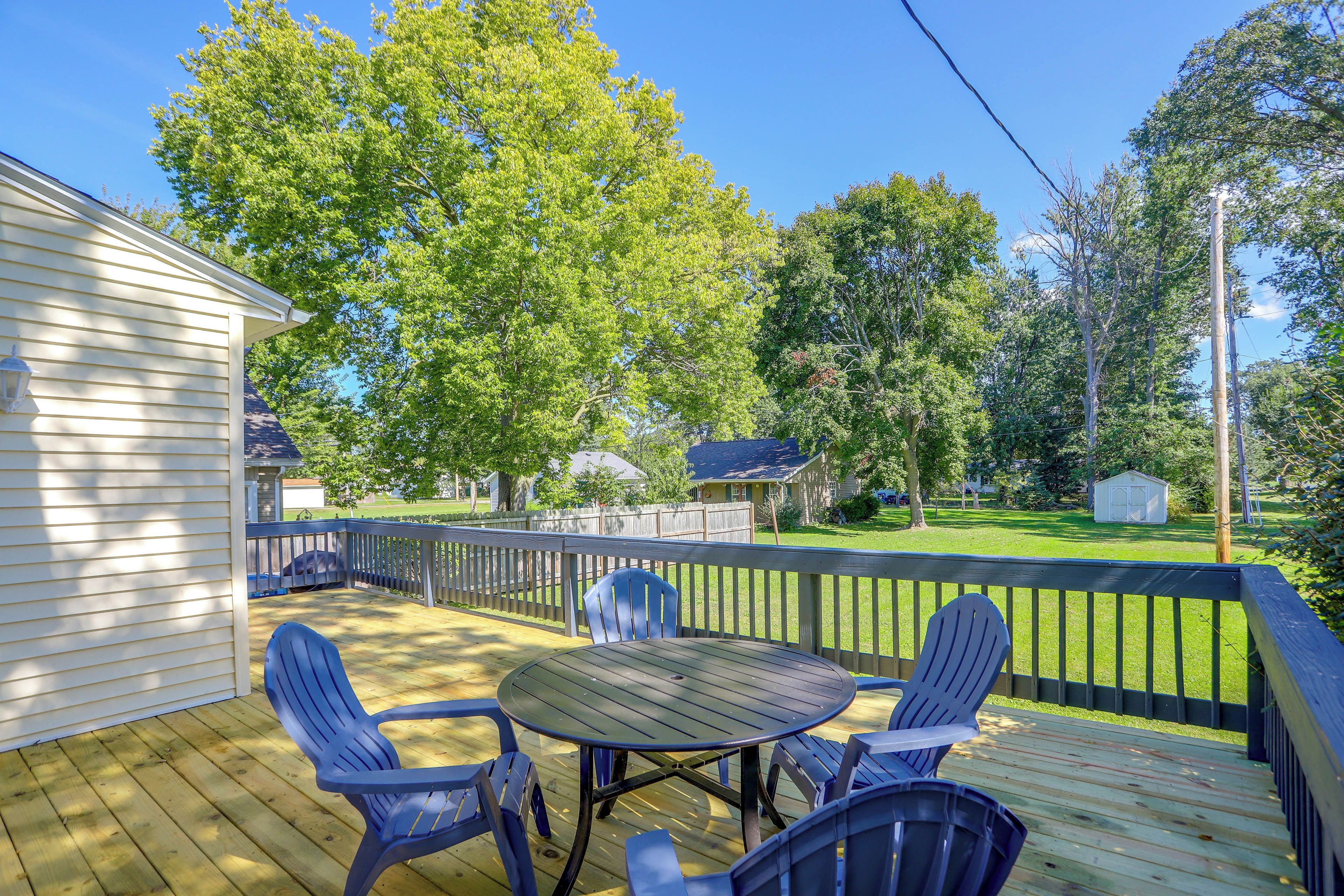 A wooden deck with a table and chairs, surrounded by a wooden fence, with houses and trees in the background.