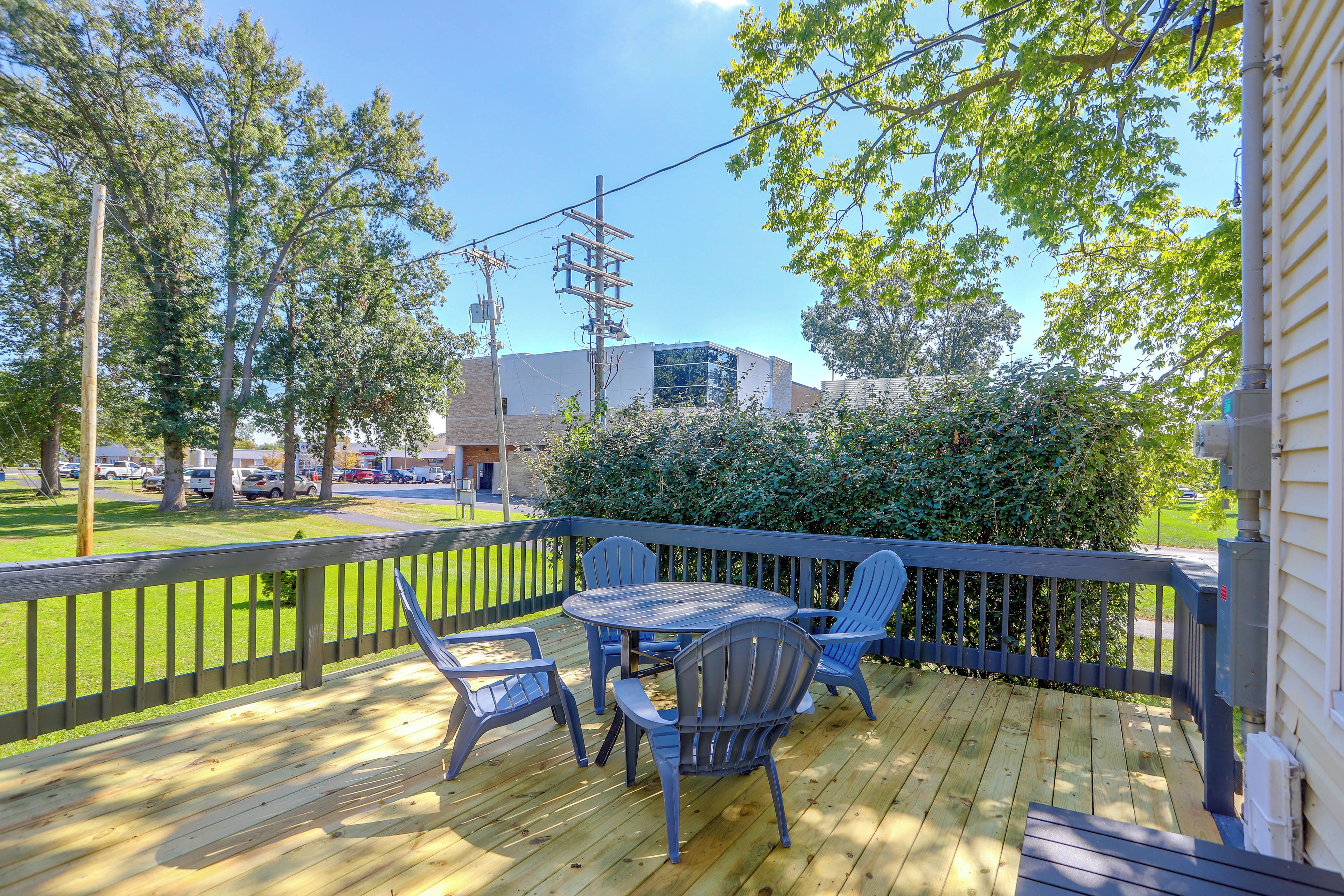 A wooden deck with a table and chairs, surrounded by a fence and trees.