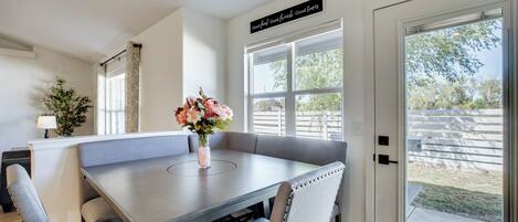A dining area with a table and chairs, a vase with flowers, and a sign above the table.