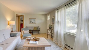 A living room with a sofa, a coffee table, a chair, a table with a plant, and a window with curtains. - Home w/ Private Yard in Rocky Point (Rocky Point)