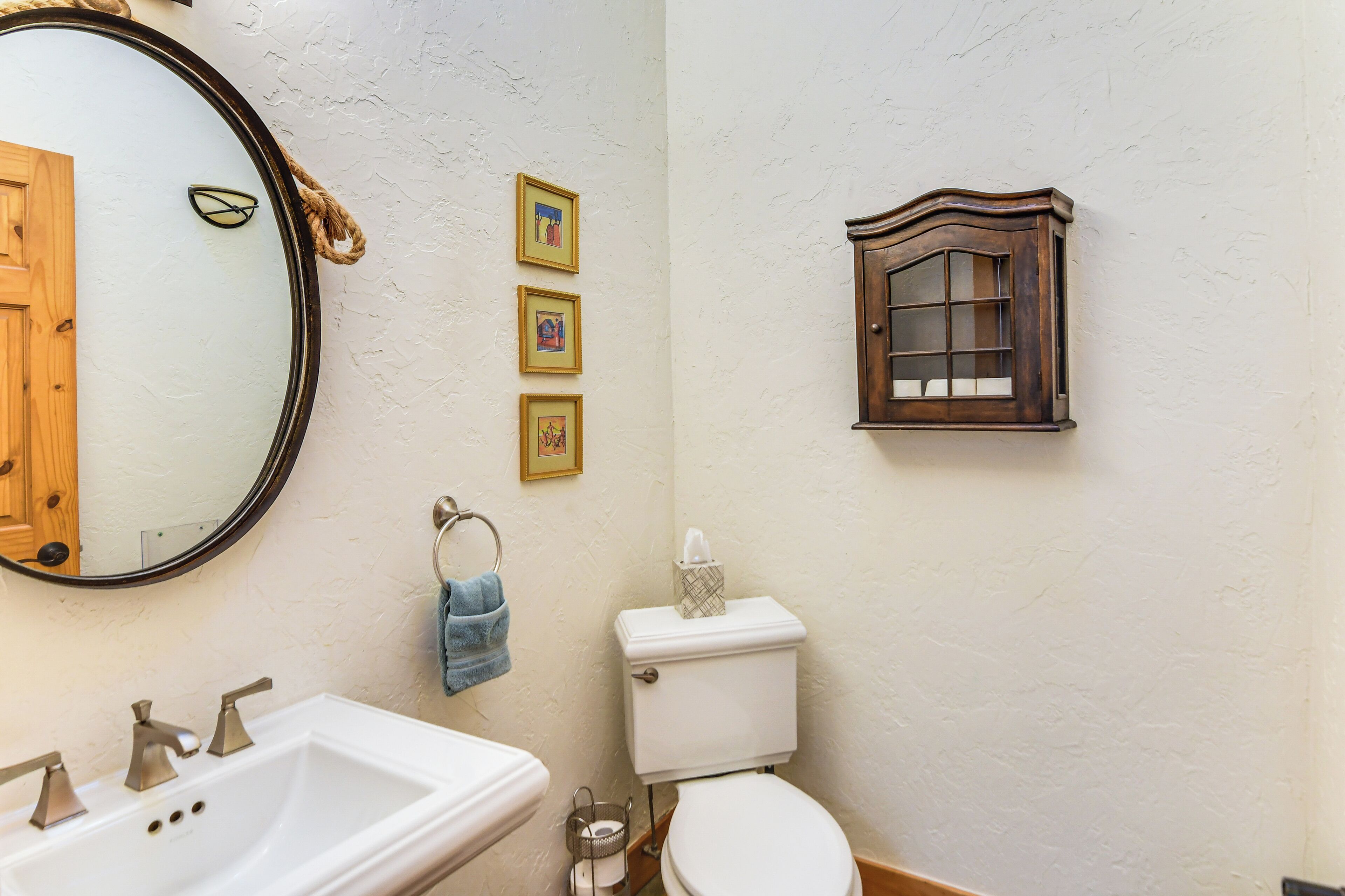 A bathroom with a white sink, a toilet, a mirror, and a wooden medicine cabinet.