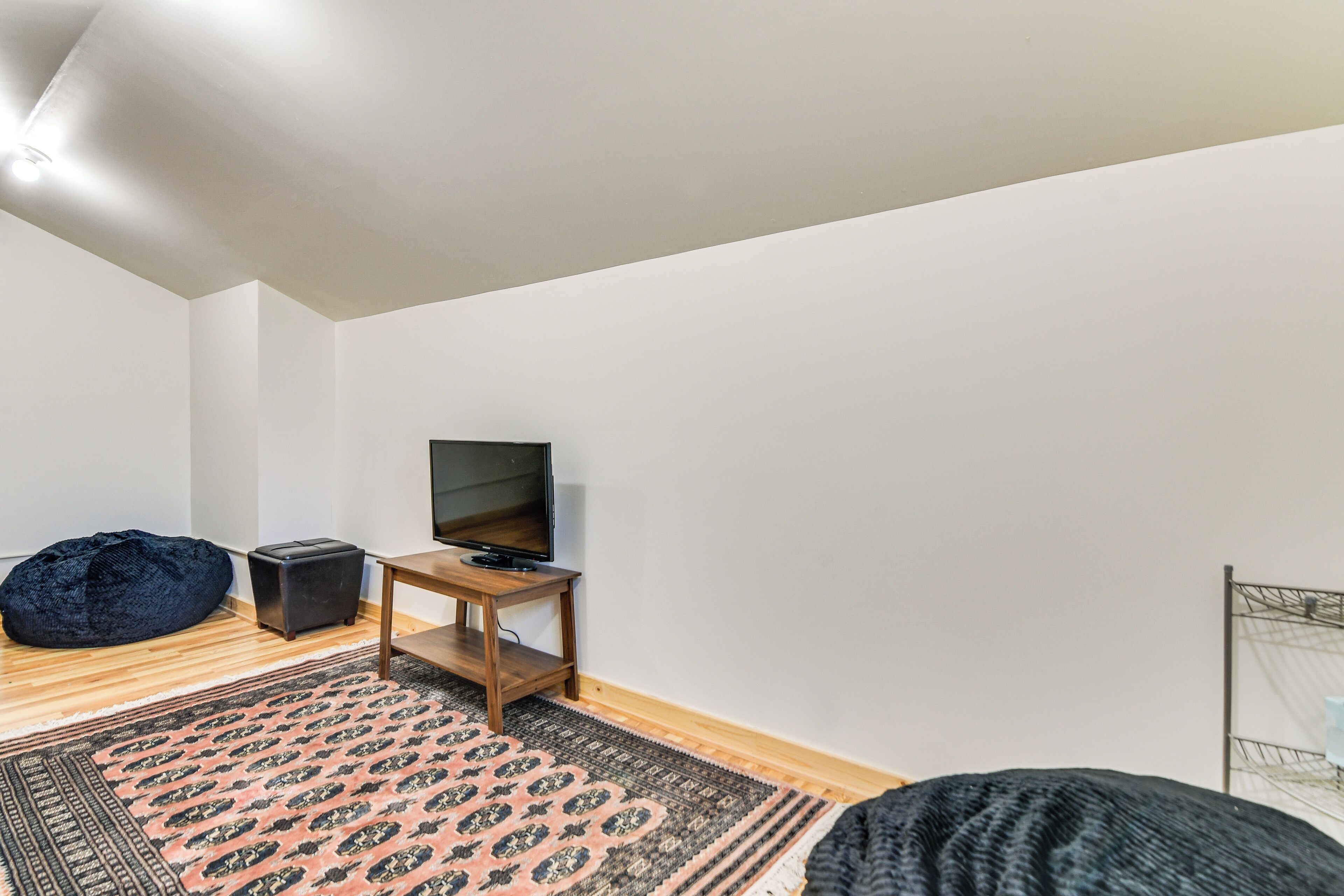 A room with a wooden floor, a black bean bag, a television on a wooden stand, and a patterned rug.