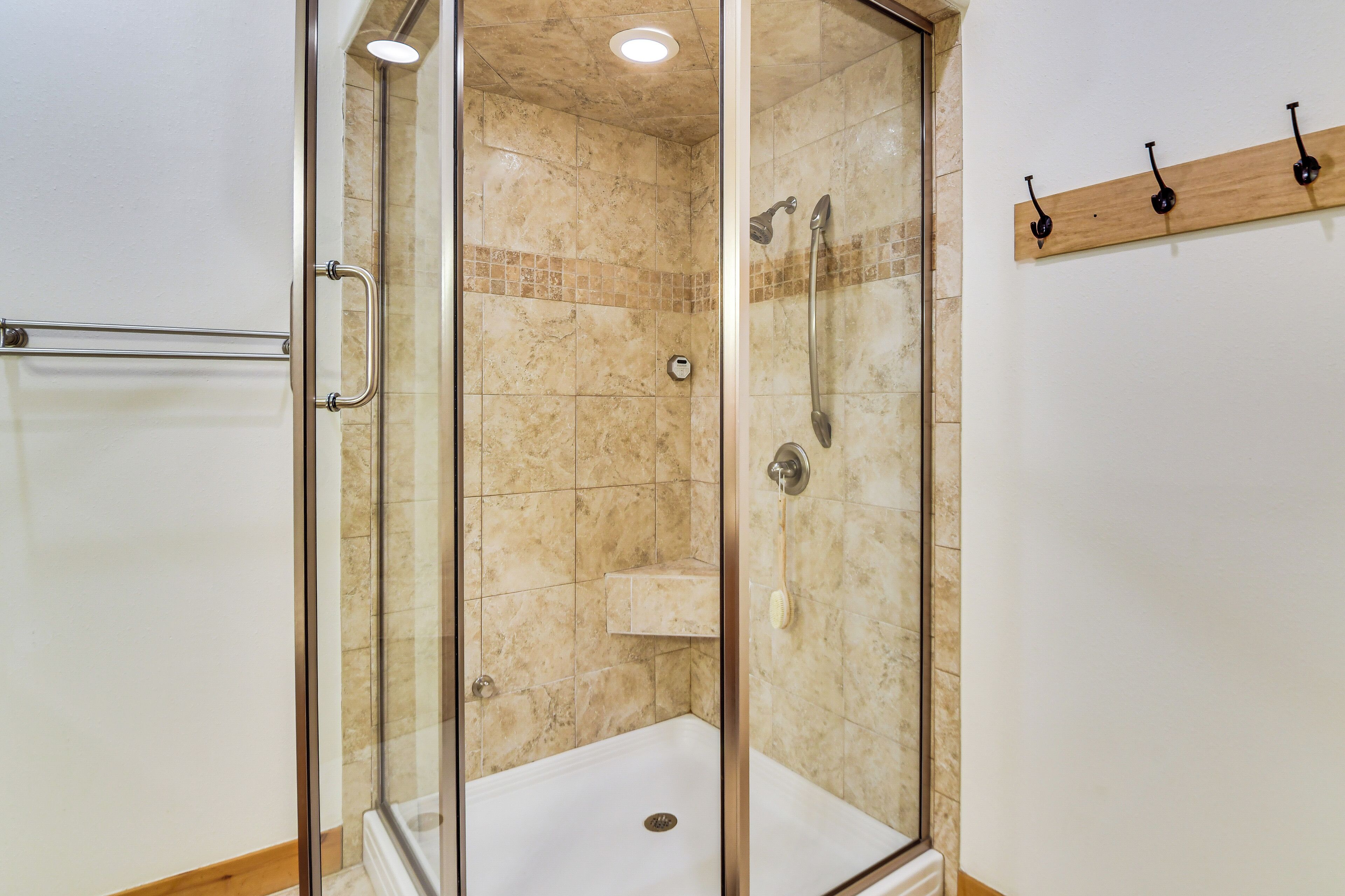 A glass-enclosed shower with a white base, beige tiles, and a wooden shelf.