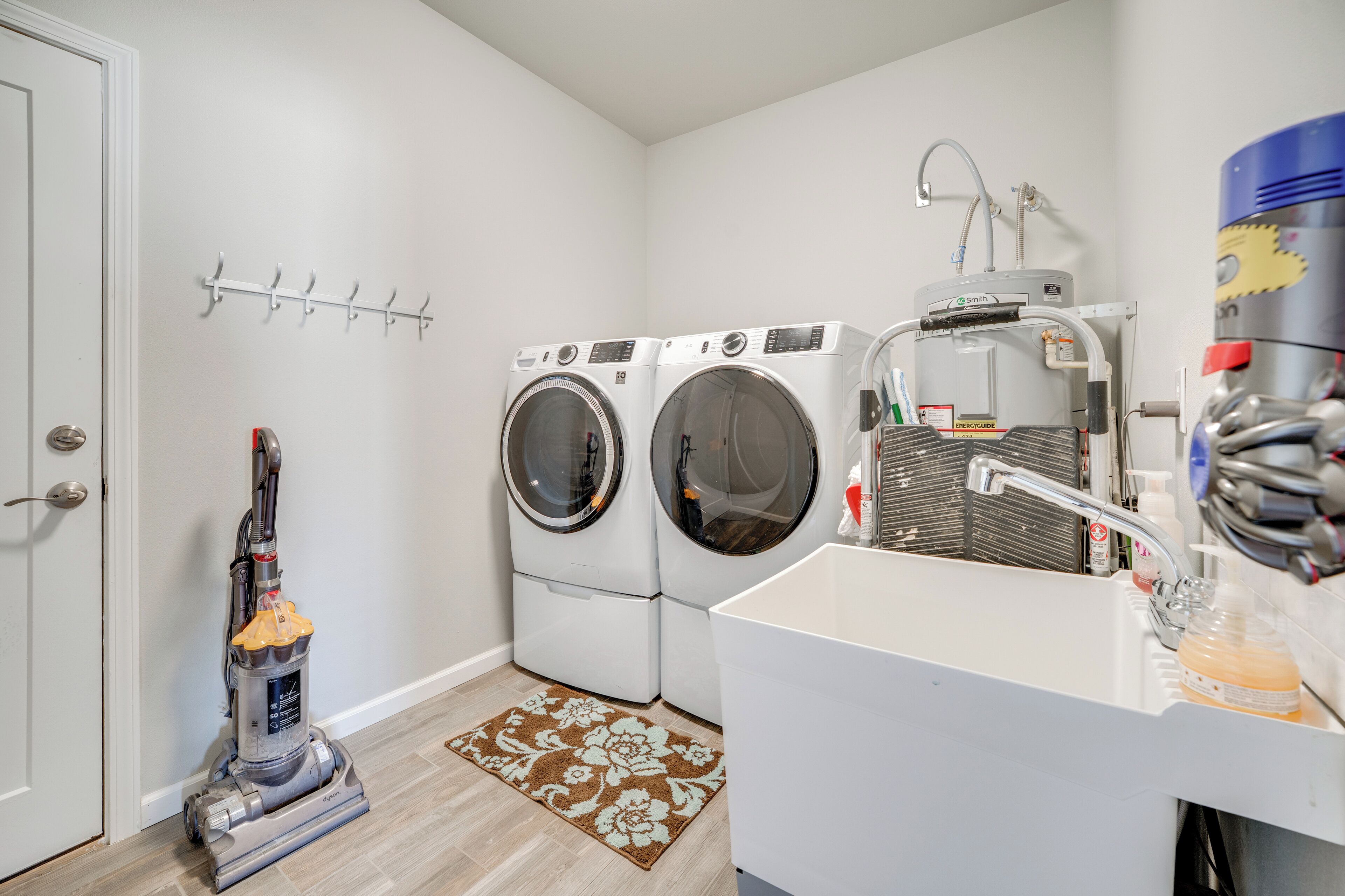 A laundry area with two front-loading washing machines, a vacuum cleaner, a sink with a soap dispenser, and a wall-mounted drying rack.