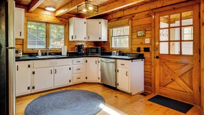 A wooden cabin kitchen with white cabinets, a black countertop, and a wooden door. - Private Spring-fed Pond: Idyllic Shrewsbury Cabin! (Shrewsbury)