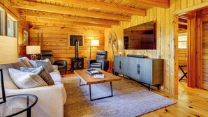 A cozy log cabin interior with a sofa, a coffee table, a TV, and a fireplace. - Private Spring-fed Pond: Idyllic Shrewsbury Cabin! (Shrewsbury)