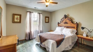 A bedroom with a wooden bed, a ceiling fan, a bedside table with a lamp, and a window with curtains. - Hiking Nearby! Mountain-view Home Outside ABQ (Edgewood)