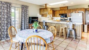 A kitchen with wooden cabinets, a refrigerator, and a dining area with a table and chairs. - Hiking Nearby! Mountain-view Home Outside ABQ (Edgewood)