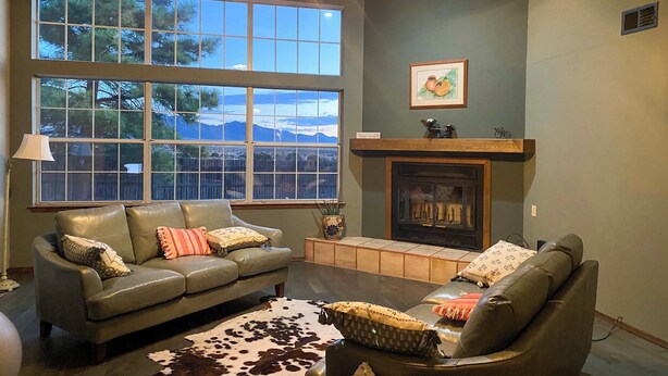 A living room with a fireplace, leather sofas, a cowhide rug, and large windows with a mountain view. - Hiking Nearby! Mountain-view Home Outside ABQ (Edgewood)