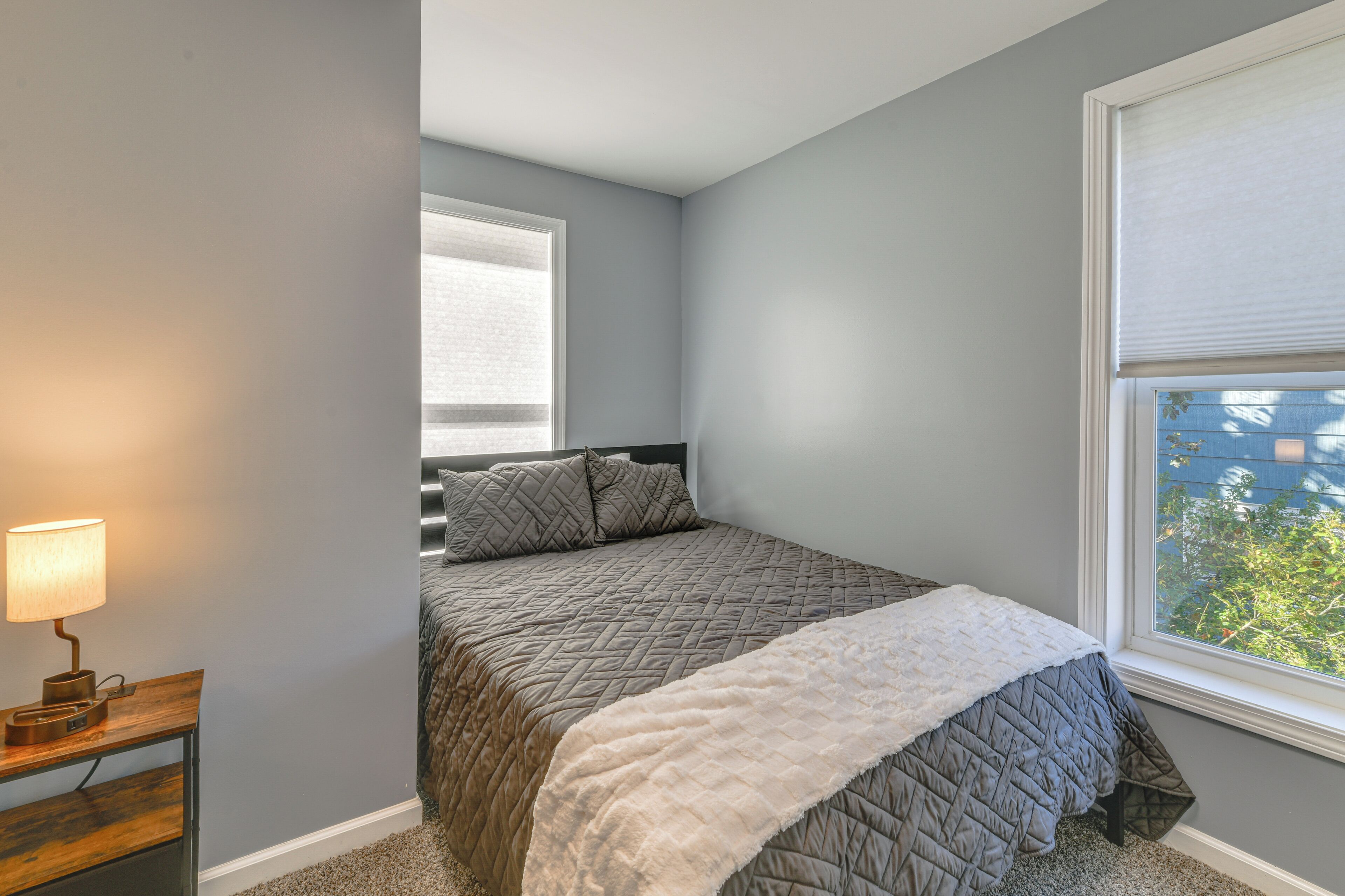 A bedroom with a bed, a nightstand, a lamp, and a window with blinds.