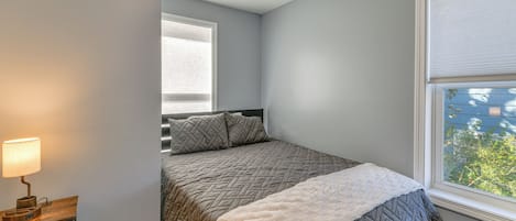 A bedroom with a bed, a nightstand, a lamp, and a window with blinds.