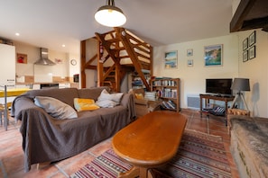 Un salon comprenant un canapé, une table en bois, une bibliothèque, un téléviseur et un escalier.