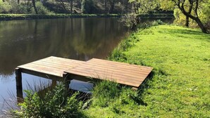 Eine hölzerne Mole, die sich in einen ruhigen See erstreckt, umgeben von üppigem Grün und Bäumen.