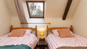 Ein Schlafzimmer mit zwei Betten, einem Fenster, einem Holzbalken an der Decke und einem Nachttisch mit Lampe.