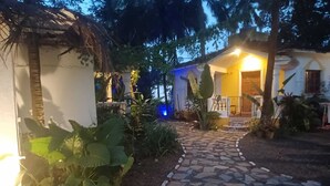 A pathway leading to a building with a thatched roof structure and a well-lit entrance.