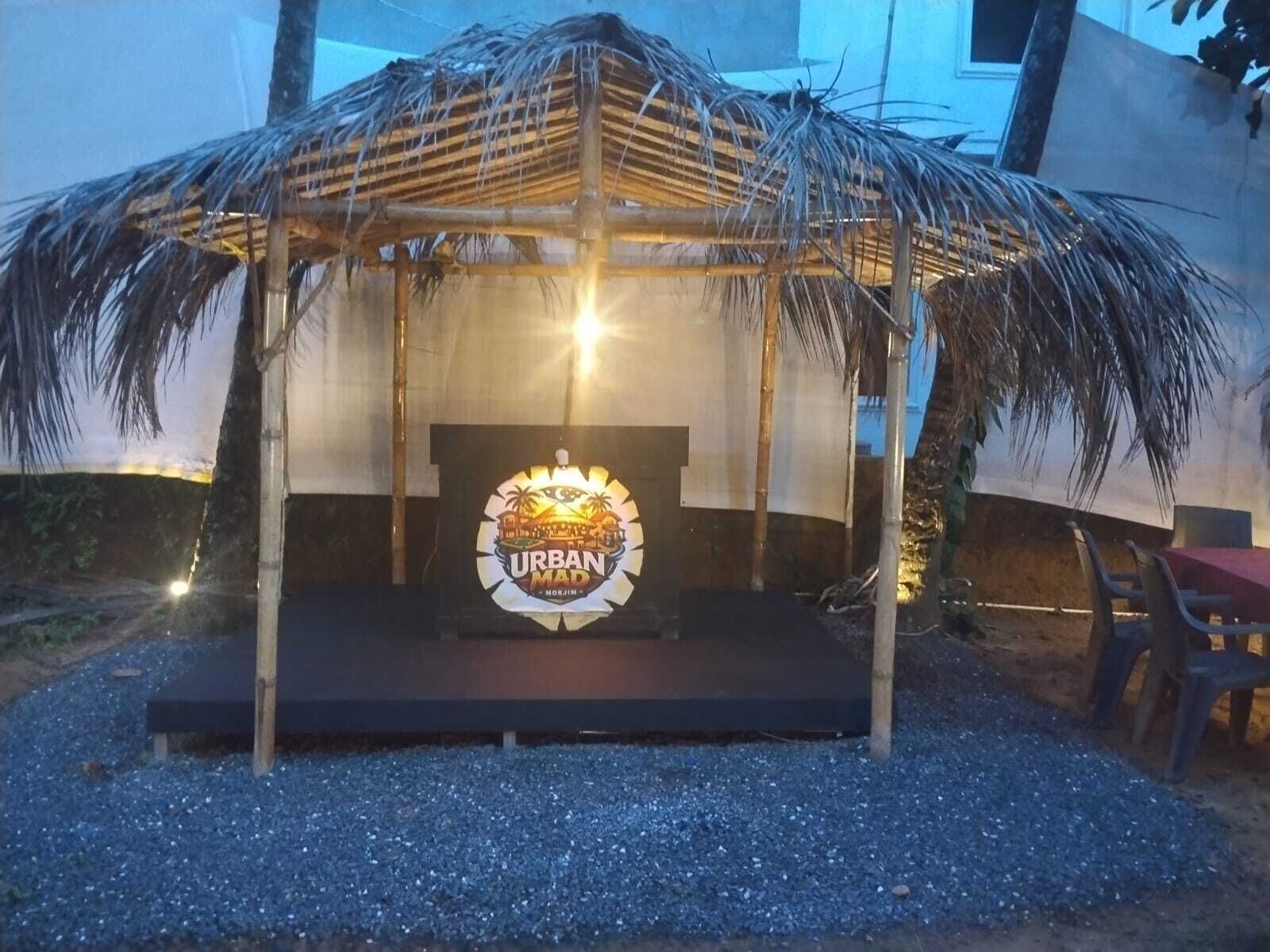 A thatched-roof structure with a logo in the center, surrounded by gravel.