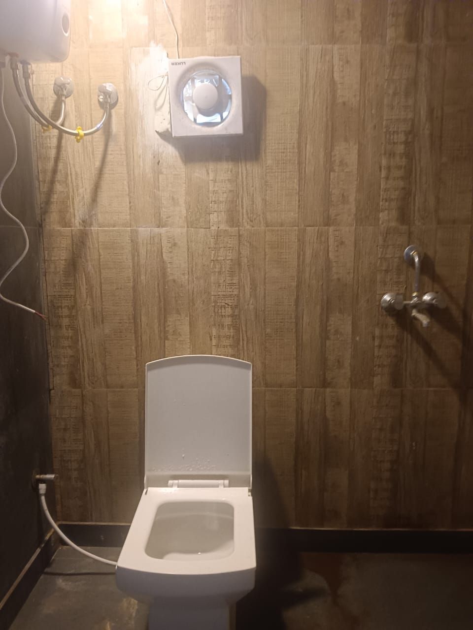 A bathroom with a white toilet, a showerhead, and a wall-mounted light fixture.