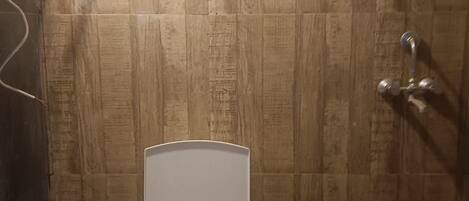 A bathroom with a white toilet, a showerhead, and a wall-mounted light fixture.