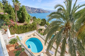A swimming pool surrounded by palm trees and a mountainous backdrop. - Villa 'El Nido' with Sea View, Wi-Fi and Air Conditioning (Almuñécar)